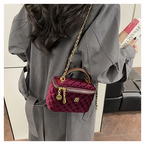 Detail of burgundy velvet quilted mini trunk bag with gold flower ornament and chain strap