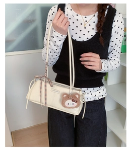 Detail of cream rectangular shoulder bag featuring a plaid ribbon and plush bear charm