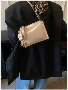Detail of beige glossy shoulder bag with golden rivets and floral charm accessory