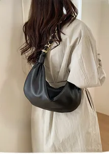 Détail d'un sac hobo noir avec chaîne dorée porté par un mannequin en trench-coat