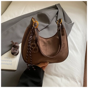 Detail of coffee brown suede hobo bag featuring woven tassels and a gold letter pendant