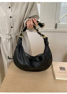 Détail du sac hobo noir avec poignée en chaîne dorée tressée posé sur une table en bois
