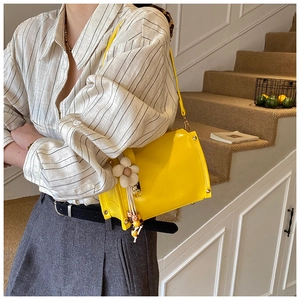 Side view of yellow shoulder bag with white flower charm and golden rivet details