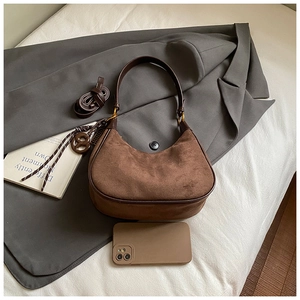 Detail of dark brown suede hobo bag with adjustable strap on a gray suit background