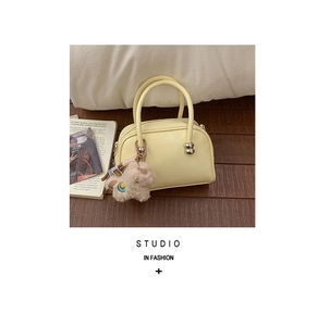 Détail d'un sac baguette jaune crème mat avec billes en métal et un charme alpaga peluche