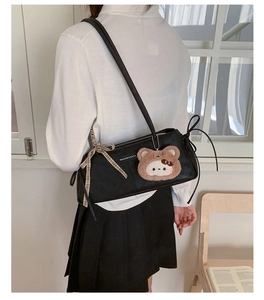 Close-up of black leather Boston bag featuring a plush bear charm and ribbon detail
