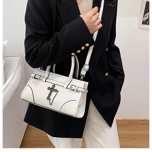 Close-up of white woven handbag with vintage metal cross charm and chain detail