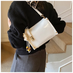 Close-up of a white leather shoulder bag with gold hardware and floral charm on a model