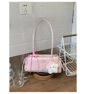 Detailed view of pink shoulder bag featuring decorative silk bow and plush cat charm