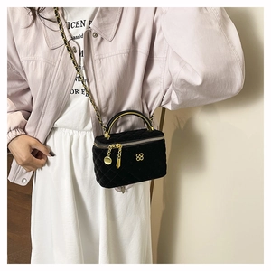 Detail of black velvet quilted handbag with gold handle and flower logo on pink blazer