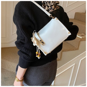 Detail of white rectangular crossbody bag with gold lock and floral bead charm decoration