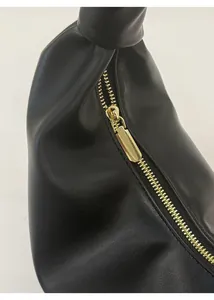 Gros plan sur la fermeture éclair en métal doré et la texture en cuir noir du sac hobo