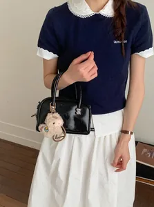 Detail einer schwarzen Lackleder-Handtasche im Boston-Stil mit Alpaka-Plüschanhänger