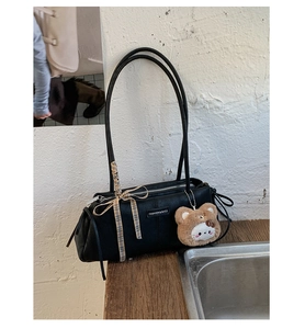 Detail of black leather underarm bag featuring a plaid bow and a cute cartoon bear charm