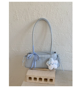 Detail of light blue baguette bag with plaid ribbon and white plush star charm on brick