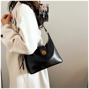 Detail of minimalist black leather hobo bag with round gold lock shown on model