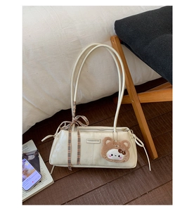 Close-up of cream underarm bag featuring a vintage plaid ribbon and plush bear charm
