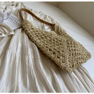 Detailed close-up of woven beige straw tote bag with brown leather strap on soft fabric
