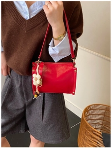 Detail of red glossy shoulder bag featuring beige floral charm and gold hardware accents