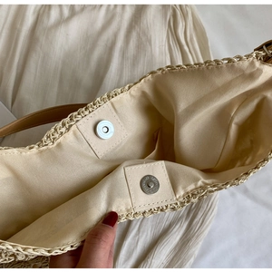 Detail of beige straw tote bag featuring interior fabric lining and metal magnetic closure