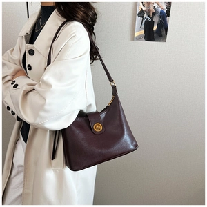 Detail view of deep brown leather hobo bag with a vintage gold twist lock on a white coat