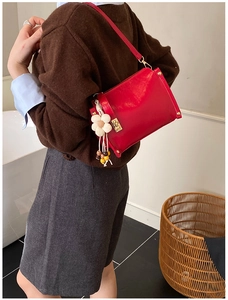 Detail of red glossy shoulder bag with white flower charm and golden hardware on model