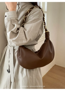 Détail du sac demi-lune en cuir marron foncé avec chaîne dorée et bandoulière en cuir tressé