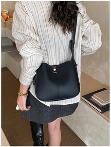 Detail of black leather bucket bag with silver lock clasp worn by a model in lifestyle setting