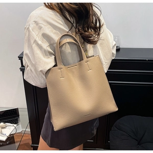 Detailed view of a light brown pebble leather tote bag worn as a shoulder bag