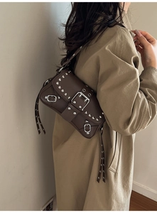Close-up of a dark brown studded underarm bag with metallic rivets and buckles on model