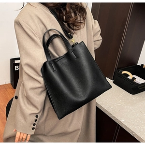 Detail of black lychee grain leather tote bag worn by a model in a beige suit jacket