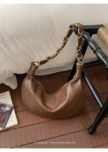 Détail d'un sac Hobo marron avec bandoulière en chaîne dorée tressée sur fond d'intérieur épuré