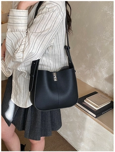Detail of black lychee grain leather bucket bag with silver metal lock and wide strap