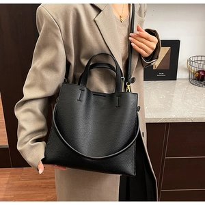 Close-up of black lychee grain leather tote bag worn with a beige trench coat for work
