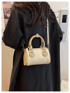 Rear view of model in black coat holding a beige canvas Boston bag with leather trim