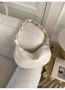 Détail du sac demi-lune crème avec bandoulière en chaîne tressée sur fond minimaliste doux