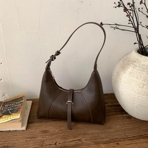 Dettaglio borsa sottobraccio marrone scuro su tavolo in legno con oggetti vintage