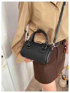 Detalle de un mini bolso Boston negro llevado como bandolera por una modelo con ropa