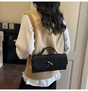 Gros plan sur la texture cuir serpent noir et le fermoir rotatif doré du petit sac
