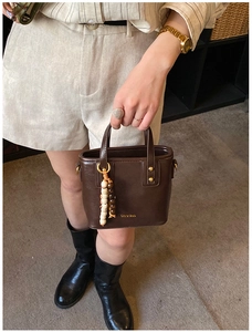 Détail du sac bandoulière en cuir marron foncé avec breloque perlée et boucles dorées