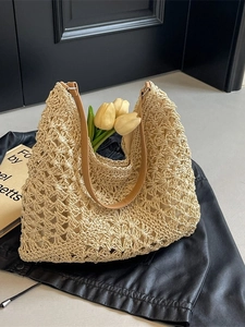 Beige woven straw tote bag with brown leather straps on a black leather jacket