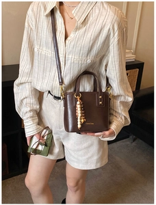Détail du sac seau marron foncé avec finition brillante, logo et breloque en perles