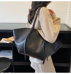 Close-up of a large black matte leather tote bag worn by a model in a minimalist setting