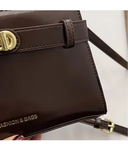 Dettaglio borsa a tracolla in pelle marrone scuro con chiusura dorata e scritte dorate