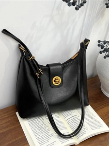 Minimalist black leather hobo bucket bag with gold hardware on a wooden table