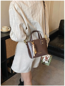 Détail du sac bandoulière en cuir marron foncé avec breloque perlée et logo