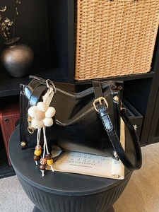 Glossy black faux leather tote with floral charm and wooden beads on a stool
