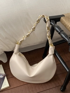 Sac demi-lune beige chic avec bandoulière en chaîne dorée sur chaise vintage