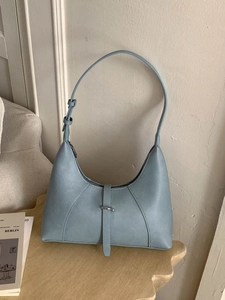 Borsa a spalla azzurra minimalista a forma di gnocco con fibbia su tavolo in legno moderno