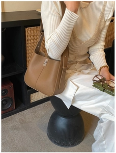 Brown leather bucket bag with silver metal clasp and adjustable strap worn on shoulder
